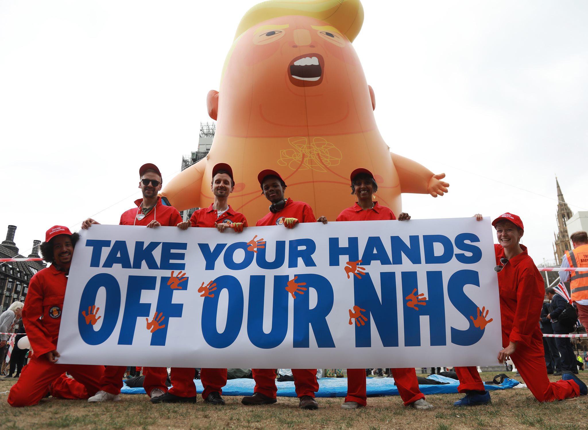 Campaigners in front of a Donald Trump blimp, holding a banner that reads "Take your hands off our NHS"
