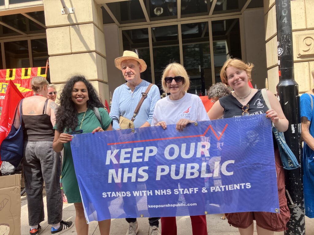 Four people pose with a banner reading 'Keep Our NHS Public stands with NHS staff and patients'