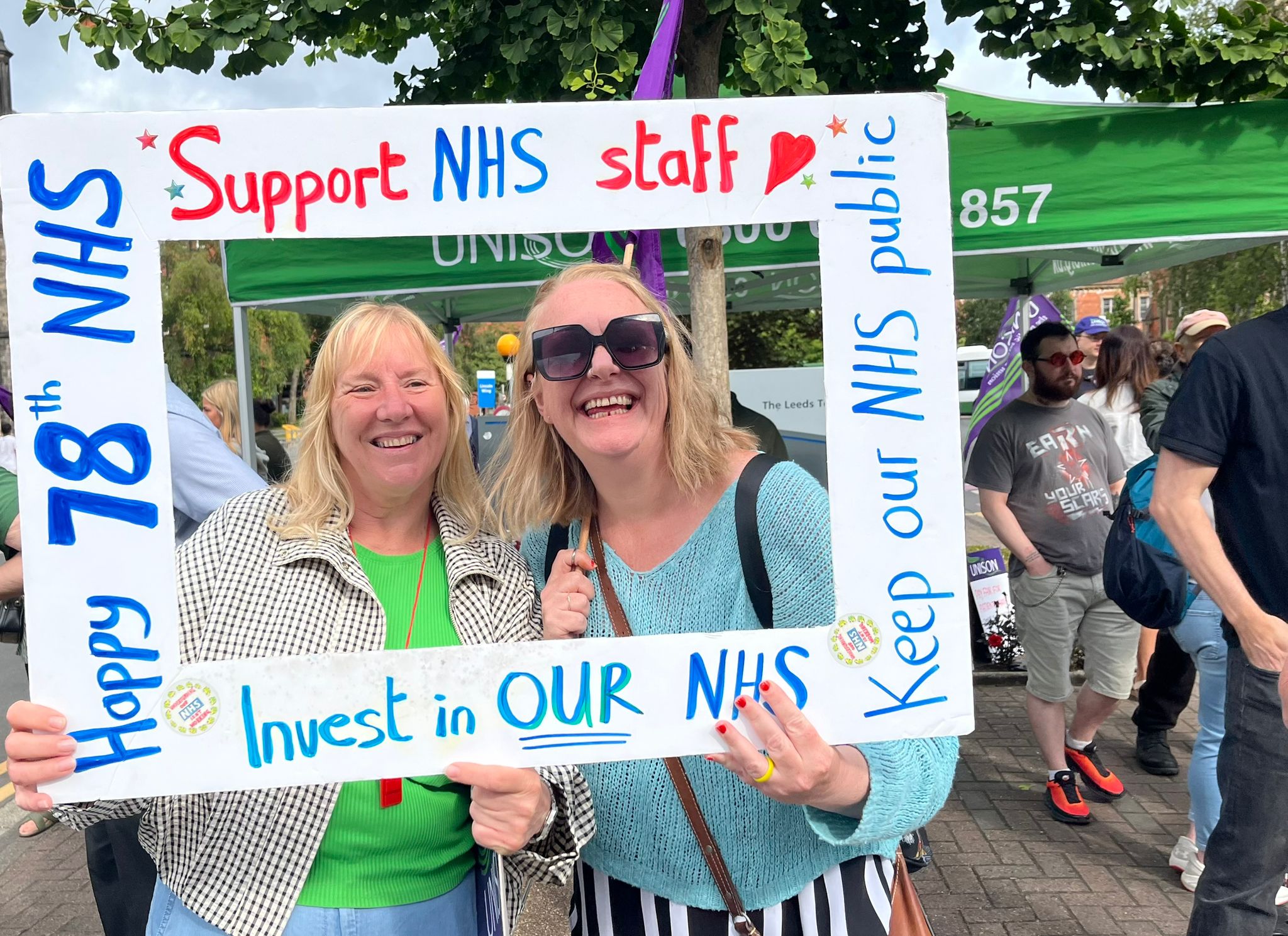 Two women pose inside a frame that reads 'Support NHS Staff' and 'Happy 78 NHS'