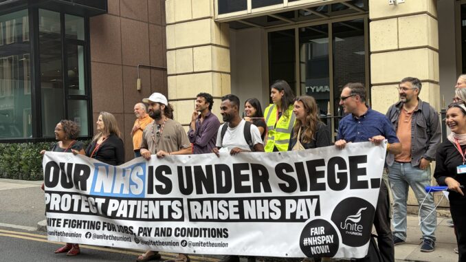 A large group of people hold a Unite the union banner in support of the NHS