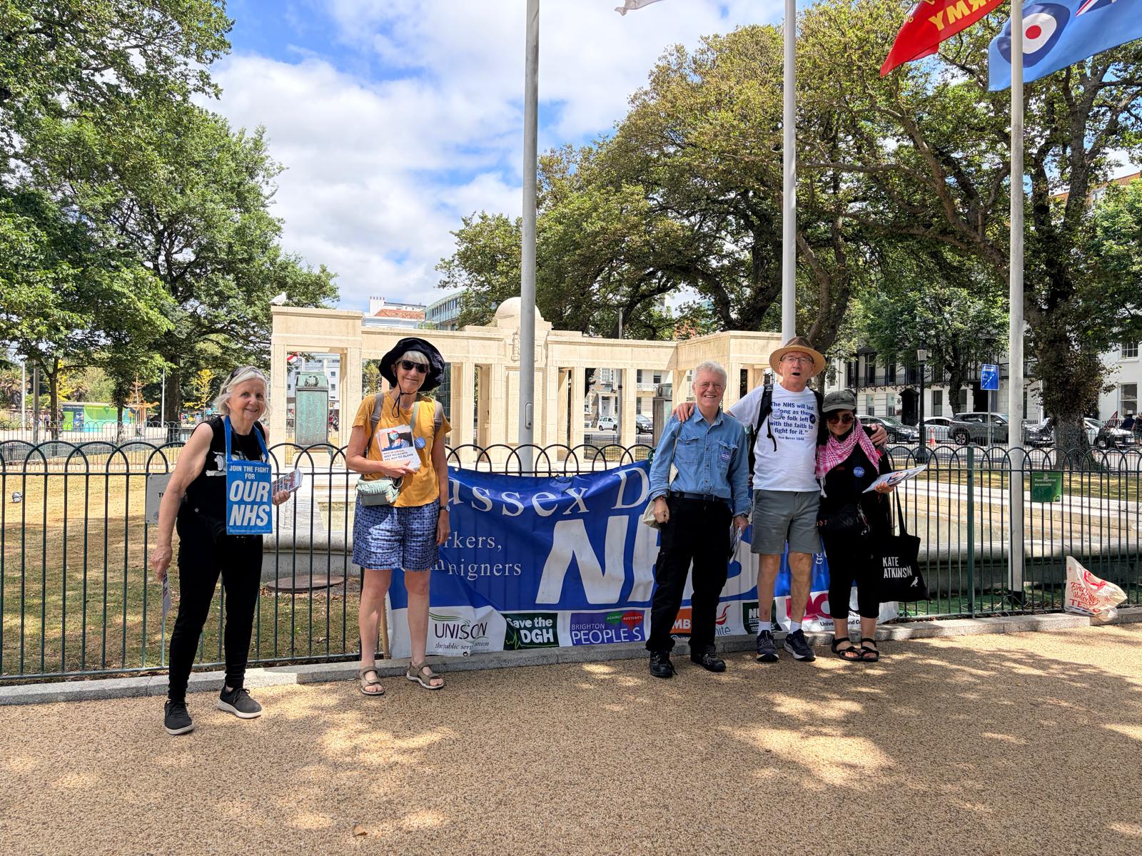Five people pose in front of a Sussex Defend Our NHS Banner